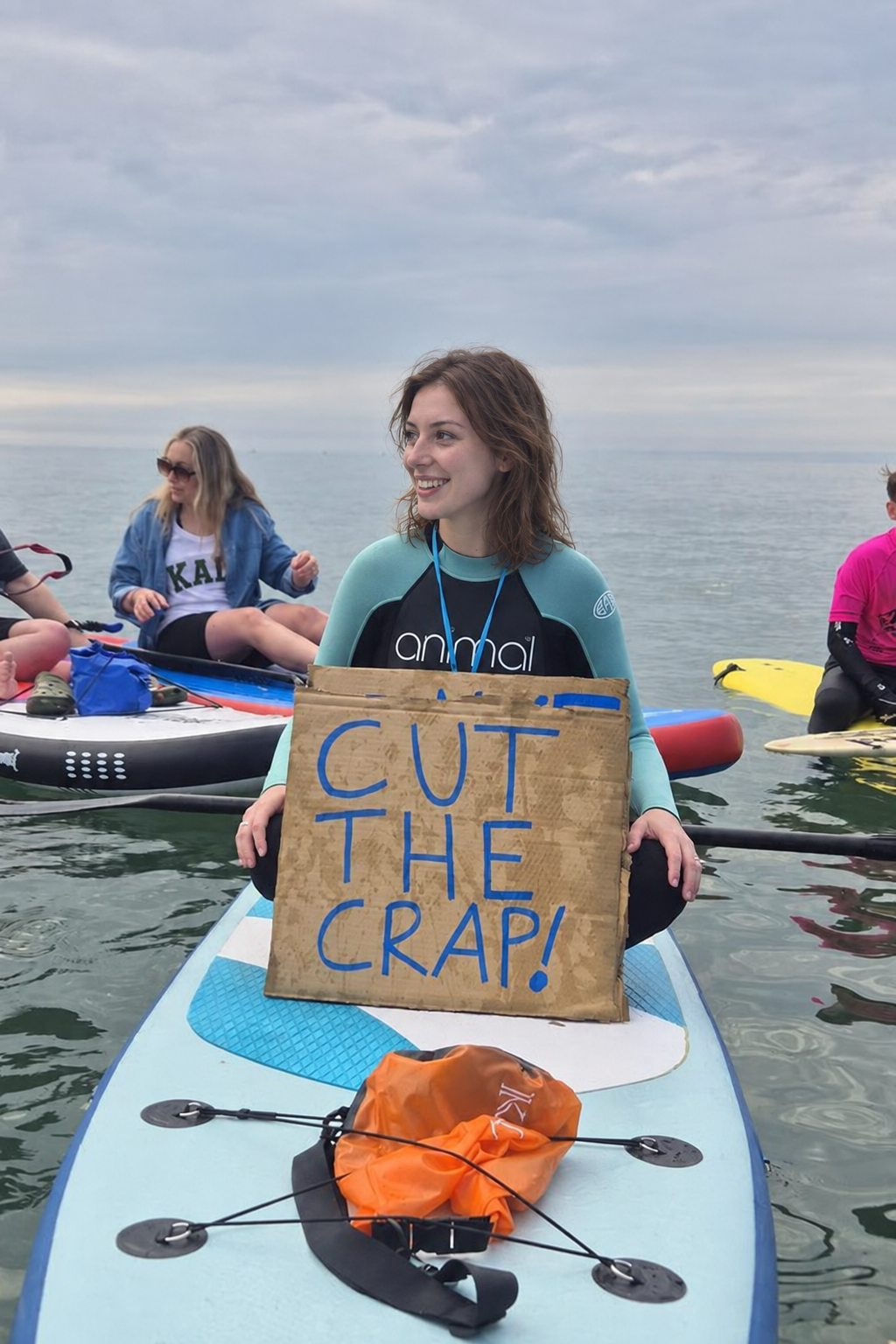 Ellie on a paddleboard holding a CUT THE CRAP placard